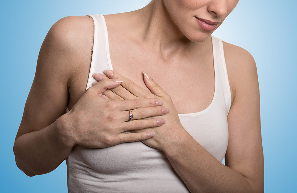 A closeup image of a woman in a white tank top with her hands against the right side of her chest.