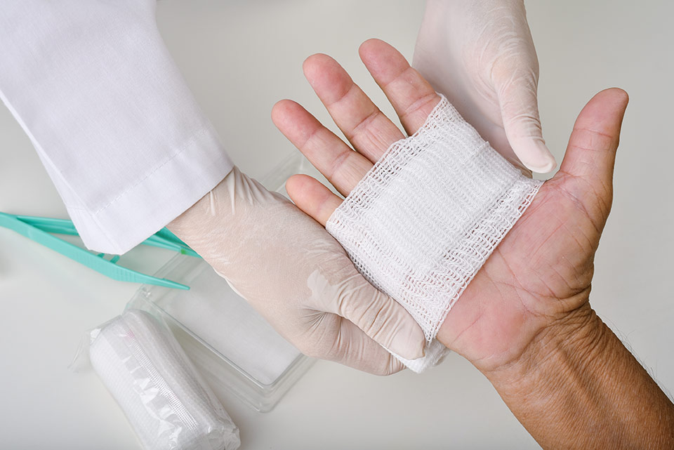 A closeup image of a doctor wrapping a patient’s hand in gauze.