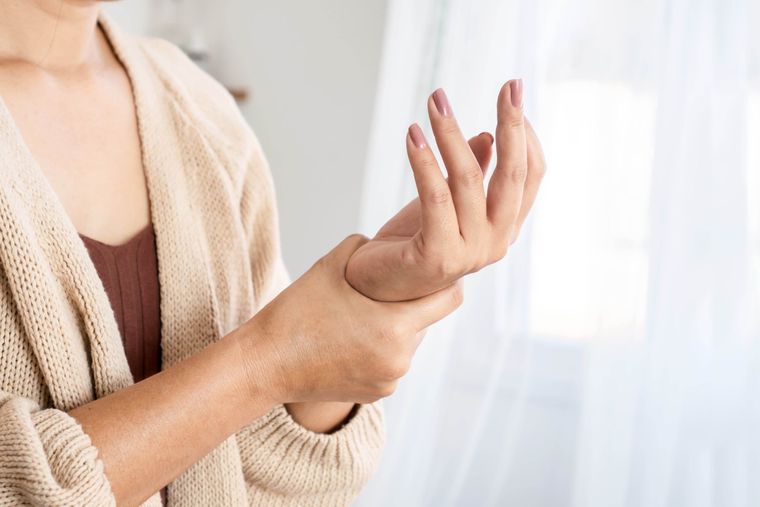 A closeup image of a woman in a cardigan gripping her wrist in pain.