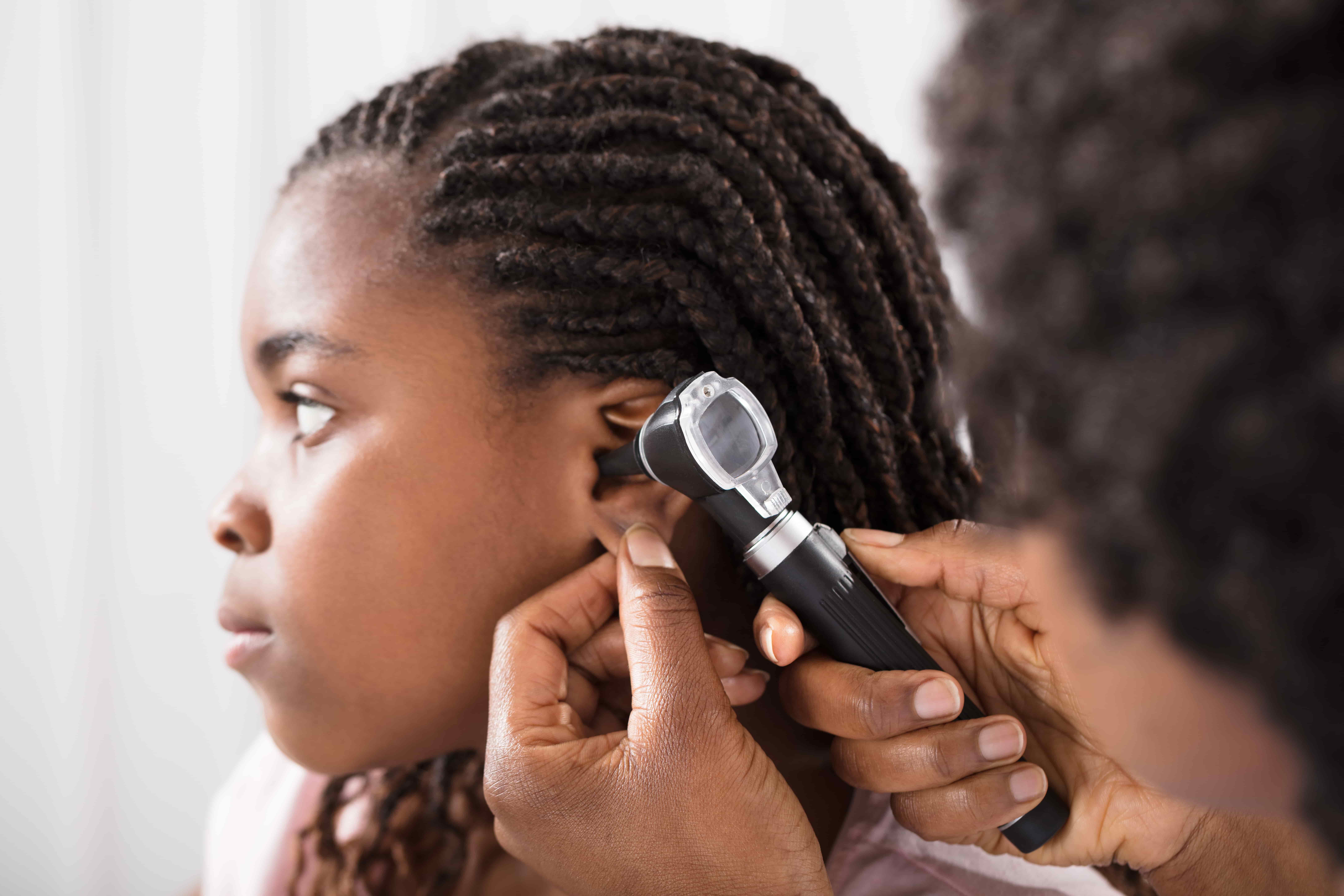 A doctor examines a young girl’s ear using an otoscope in a medical office.